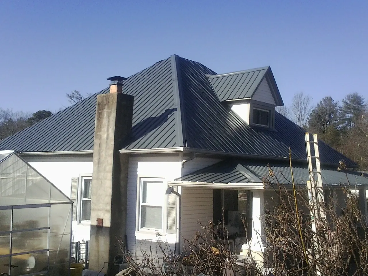 Dark blue standing seam metal roof on a white farmhouse with dormer — Slate & Tile Roof Repair by Roofing Brothers in Prophetstown