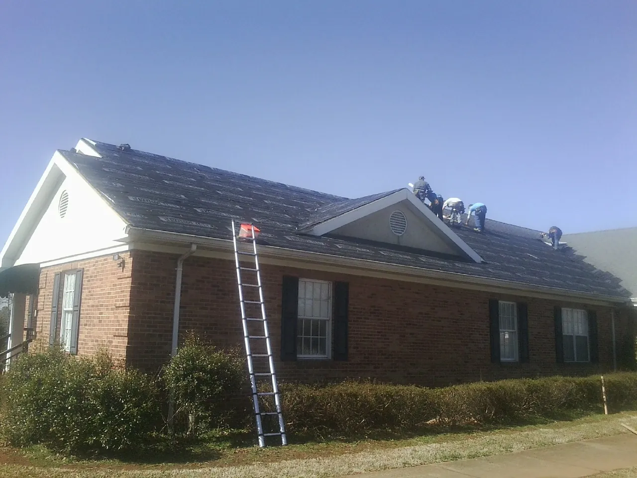 Crew tearing shingles off a brick ranch roof with a ladder set — Emergency Roof Repair work by our crew in Prophetstown