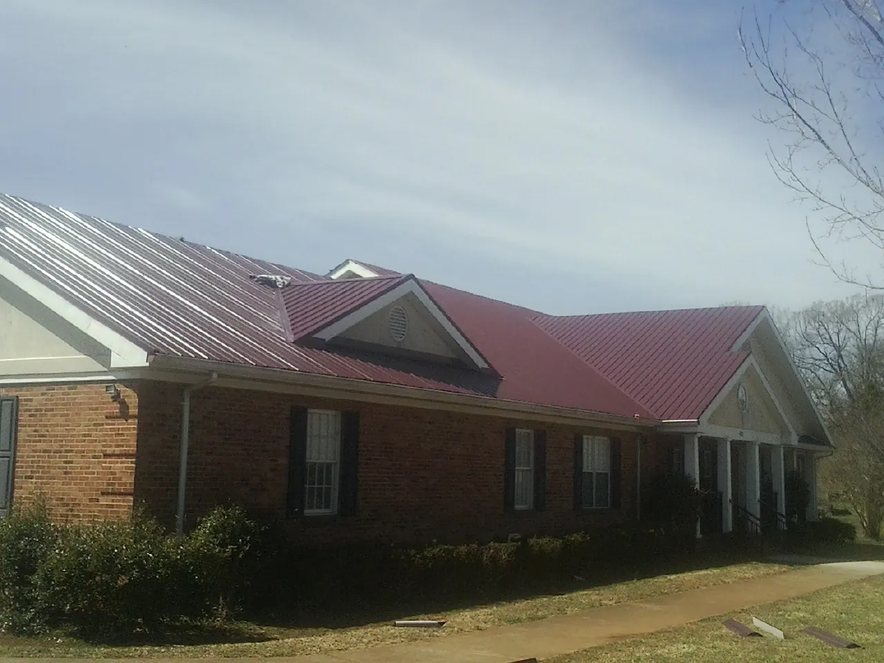 Red metal roof with gabled entries on a long brick building, from a Hail Damage Roof Repair job in Prophetstown