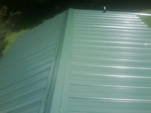 New green metal panels meeting at the ridge of a roof — Flat Roof Repair work by our crew in Prophetstown