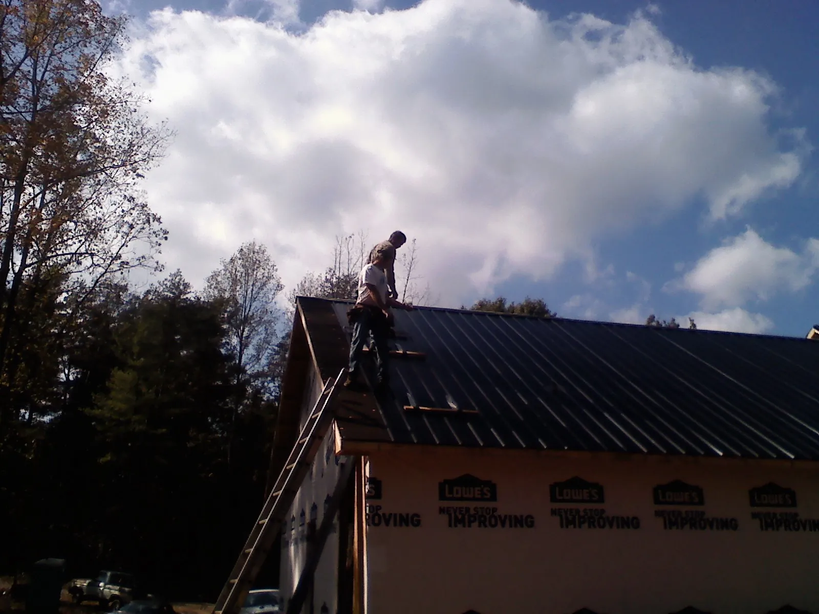 Roofer fastening dark metal panels high against a cloudy sky, from a Roof Inspection job in Prophetstown