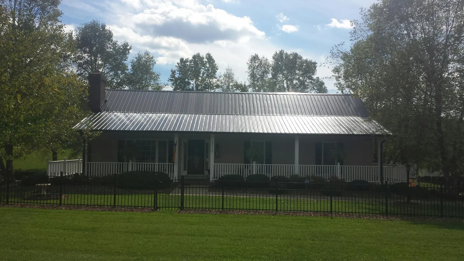 Gray metal roof on a brick ranch with a full width front porch — Gutter Guard Installation work by our crew in Prophetstown