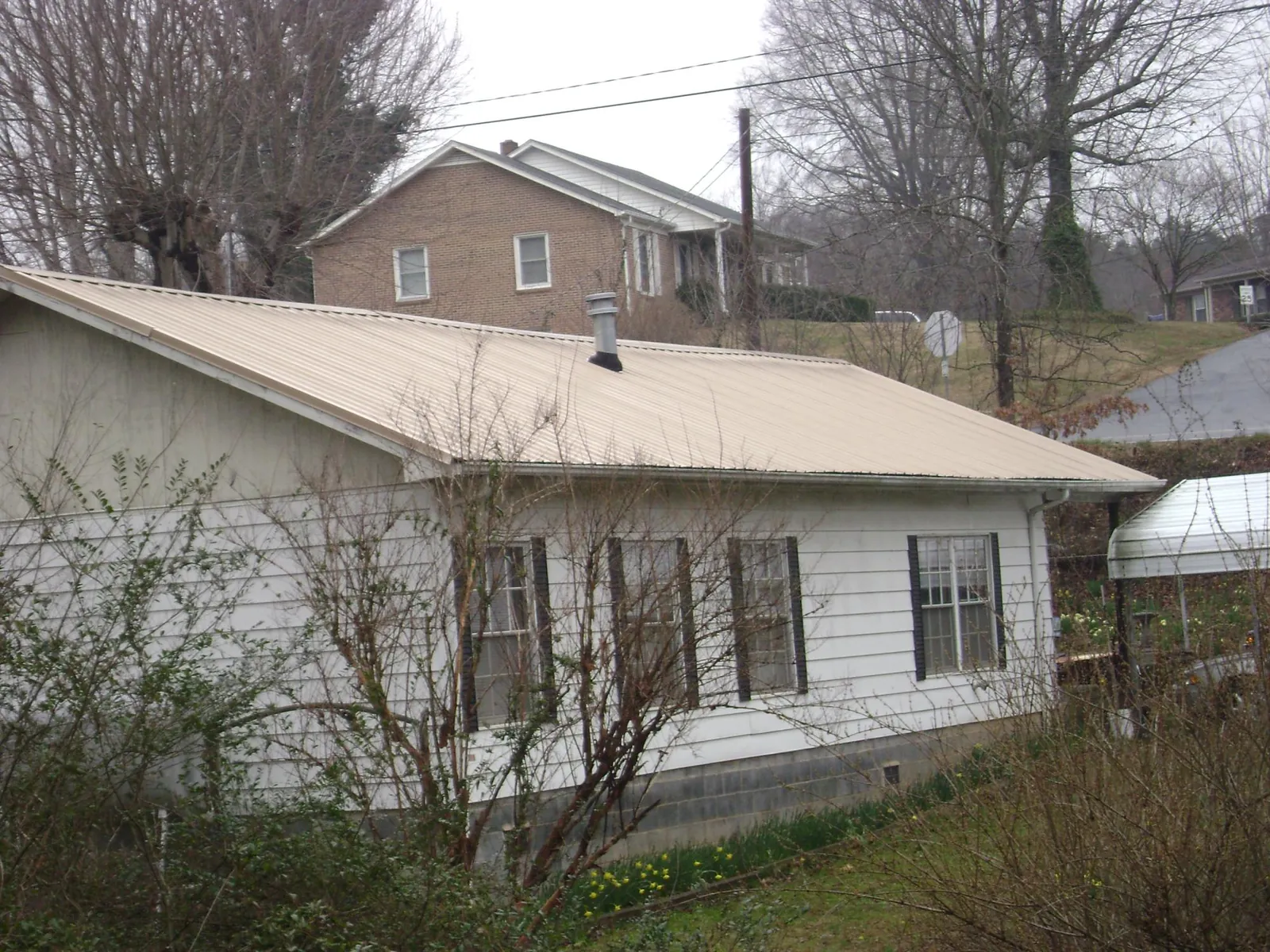 Tan metal roof on a white sided house set into a hillside — Commercial Roofing by Roofing Brothers in Prophetstown