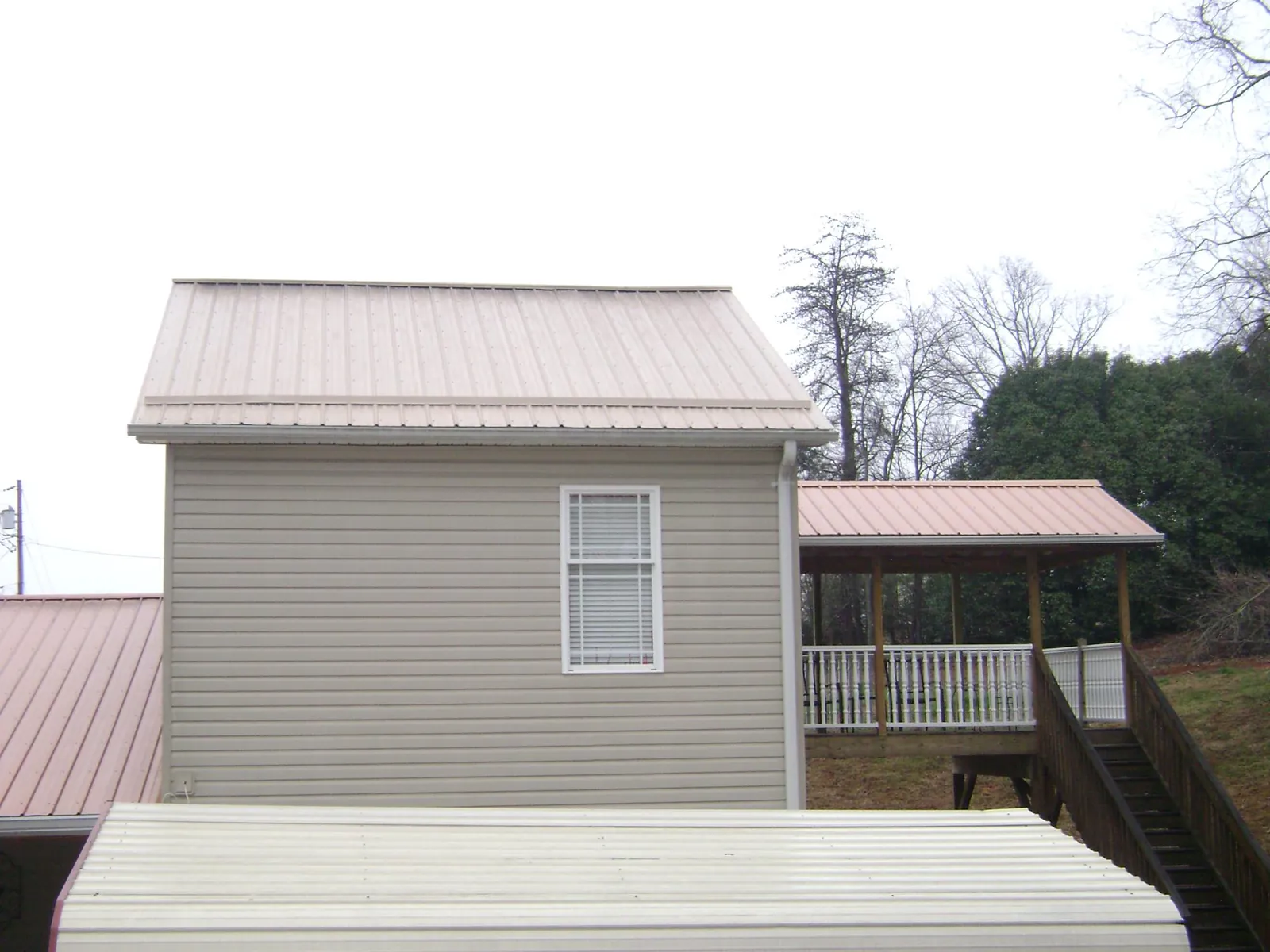 Tan metal roofs on a two story addition and attached porch, from a Roof Replacement job in Prophetstown